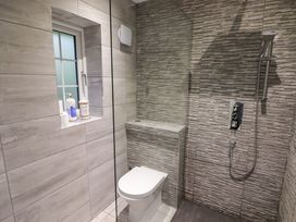 A bathroom with a toilet next to a walk-in shower and a small window with toiletry bottles on the ledge at Hiraeth in Cwmtaf near Cefn-Coed-Y-Cymmer