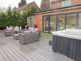 An outdoor patio with wicker furniture including a sofa and chairs with purple cushions a hot tub and glass sliding doors leading inside at Hiraeth in Cwmtaf near Cefn-Coed-Y-Cymmer