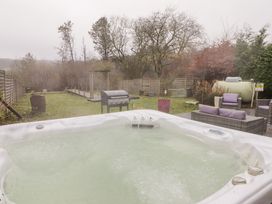 An outdoor hot tub with water flowing near a barbecue grill and patio furniture in a fenced backyard at Hiraeth in Cwmtaf near Cefn-Coed-Y-Cymmer
