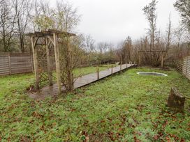 A grass garden with a wooden pergola walkway a trampoline and a wooden swing set at Hiraeth in Cwmtaf near Cefn-Coed-Y-Cymmer