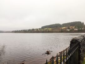 A lake with wooded hills and houses in the background and a black iron fence in the foreground at Hiraeth in Cwmtaf near Cefn-Coed-Y-Cymmer
