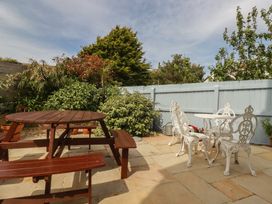 A garden with a wooden table and white chairs at Carpe Diem in Crantock