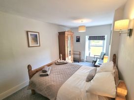 A bedroom with a wooden bed with folded towels and pillow a wooden wardrobe an armchair and a window at Moelwyn View Cottage in Llan Ffestiniog