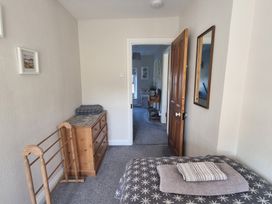 A bedroom with a bed covered in patterned bedding and towels a wooden dresser with a folded blanket and a clothes drying rack next to it and an open door showing a hallway at Moelwyn View Cottage in Llan Ffestiniog