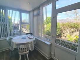 A dining area with a round table and three chairs next to large windows and a glass door at Moelwyn View Cottage in Llan Ffestiniog