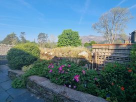 A garden with flowers bushes and trees with mountains in the background at Moelwyn View Cottage in Llan Ffestiniog