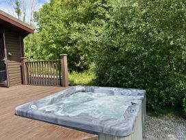 A hot tub on a deck surrounded by trees at Willow Lodge in Constantine near Falmouth