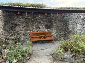 An outdoor seating area with a wooden bench and stone wall at Garth Cottage Groes near Denbigh