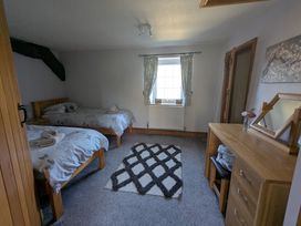 A bedroom with two single beds a window with curtains a wooden chest of drawers and a mirror at Gwrtheyrn in Dyffryn Ardudwy
