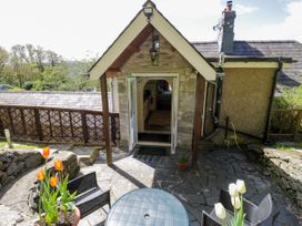 An outdoor patio area with a round table and chairs near a stone building with open double doors at The Nook in Maenan