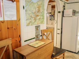 A small kitchen area with a wooden table and chairs a map on the wall a sink visible through an arched doorway and a refrigerator with a microwave on top at The Nook in Maenan