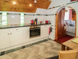 A kitchen with white cabinets and black countertop next to an arched doorway leading to a bedroom at The Nook in Maenan