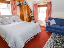 A bedroom with a bed covered in gray bedding a blue sofa a wooden wardrobe two windows with red curtains and a red carpet at The Nook in Maenan