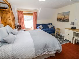 A bedroom with a bed, a blue sofa, a wooden wardrobe, a window with curtains, a desk, and a painting on the wall at The Nook in Maenan