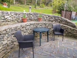 An outdoor seating area with two black chairs and a round table by a stone wall with potted flowers at The Nook in Maenan