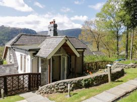 A stone cottage with a tiled roof and open door next to stone walls and grass at The Nook in Maenan