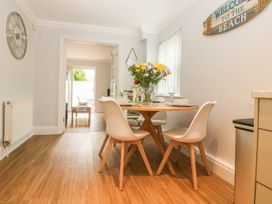 A dining area with a round wooden table and four white chairs a wall clock and a welcome sign on the walls at 7 The Retreat in Paignton