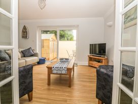 A living room with a sofa, coffee table, television on a wooden stand, and sliding glass doors at 7 The Retreat in Paignton
