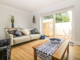 A living room with a beige sofa and pillows a wooden coffee table with a blue and white runner and bowl a sliding glass door showing a patio with chairs and a wooden shed at 7 The Retreat in Paignton