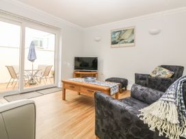 A living room with a wooden coffee table black armchairs a TV on a stand and glass patio doors at 7 The Retreat in Paignton