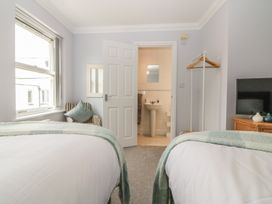A bedroom with two beds facing an open door to a bathroom and a TV on a wooden cabinet at 7 The Retreat in Paignton