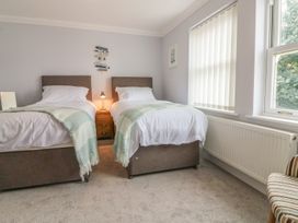 A bedroom with two single beds a bedside table with a lamp a window with blinds and a striped chair at 7 The Retreat in Paignton