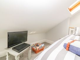 A TV on a small table with a DVD player and a basket of DVDs next to a bed in a room with a skylight at 7 The Retreat in Paignton