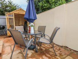An outdoor patio with a glass table and four chairs a blue umbrella and a wooden shed at 7 The Retreat Paignton