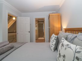 A bedroom with a bed featuring multiple pillows a wooden wardrobe an open door showing a hallway and another open door leading to a bathroom with a shower at 7 The Retreat in Paignton