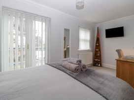 A bedroom with a bed with folded towels a desk a mounted TV and a tall triangular corner shelf at 7 The Retreat in Paignton