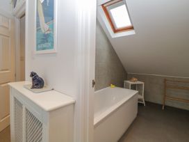 A bathroom with a bathtub under a skylight window a small white wicker table with a seashell and a wooden towel rack at 7 The Retreat in Paignton