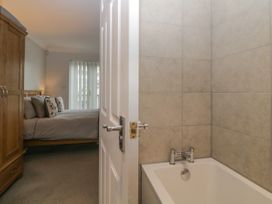 A bedroom with a bed and pillows next to a wooden wardrobe with a bathtub and tiled wall visible through an open door at 7 The Retreat in Paignton