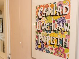 A framed poster on the wall with the text 'Cariad Uwchlaw Popeth' in a hallway at The Coach House Llangollen