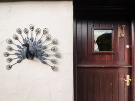 A metal peacock wall decoration next to a dark wooden door with a small window at Hafoty Boeth Cottage in Corwen