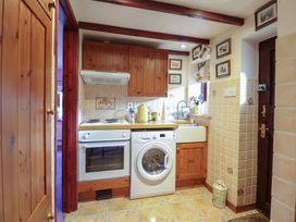 A small kitchen with wooden cabinets a washing machine an oven a tiled floor and walls at Hafoty Boeth Cottage in Corwen