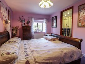 A bedroom with a wooden bed and floral bedding a chest of drawers and a window with sheer curtains at Hafoty Boeth Cottage in Corwen