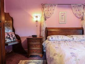 A bedroom with a wooden bed and bedside table with a chair and pink walls at Hafoty Boeth Cottage in Corwen