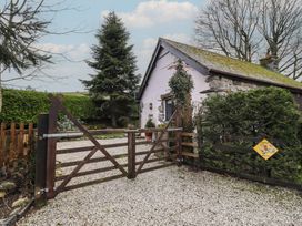 A wooden gate on a gravel driveway beside a stone and white cottage with greenery at Hafoty Boeth Cottage in Corwen