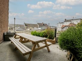 An outdoor patio area with a wooden picnic table bench seating wicker chairs and surrounding greenery at Eversley in Llandudno