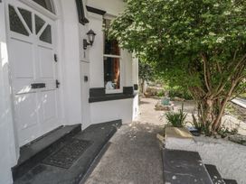 An entrance to a white house with a black doormat a black and white step a tree and plants in the garden at Eversley in Llandudno