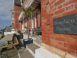 The exterior entrance of a brick building with steps a bench potted plants and a sign reading Beaulieu House in Llandudno