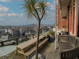 An outdoor terrace with wooden bench and picnic table near red brick building overlooking town and hills at Beaulieu House in Llandudno