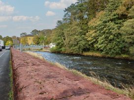 A river with a stone wall and road beside it at Riverside Cottage in Cockermouth