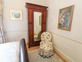 A bedroom with a wardrobe and floral chair at Maple Cottage in Buckland Newton near Dorchester