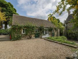 A stone building with a tiled roof and climbing plants near a gravel area at Hazel Manor Wing in Painswick