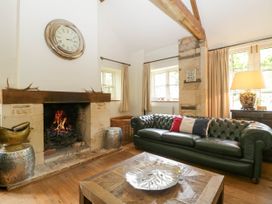 A living room with a fireplace a clock a leather sofa and a wooden coffee table at Hazel Manor Wing in Painswick