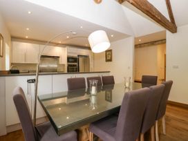A dining area with a glass table and six chairs next to a kitchen with white cabinets and stainless steel appliances at Hazel Manor Wing in Painswick