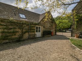A gravel courtyard with a stone building climbing plants and a white door at Hazel Manor Wing in Painswick