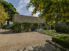A stone building with climbing plants and a gravel courtyard with trees and shrubs at Hazel Manor Wing in Painswick