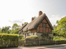 A thatched cottage with trees and a fence at Elmhurst Cottage in Lower Quinton
